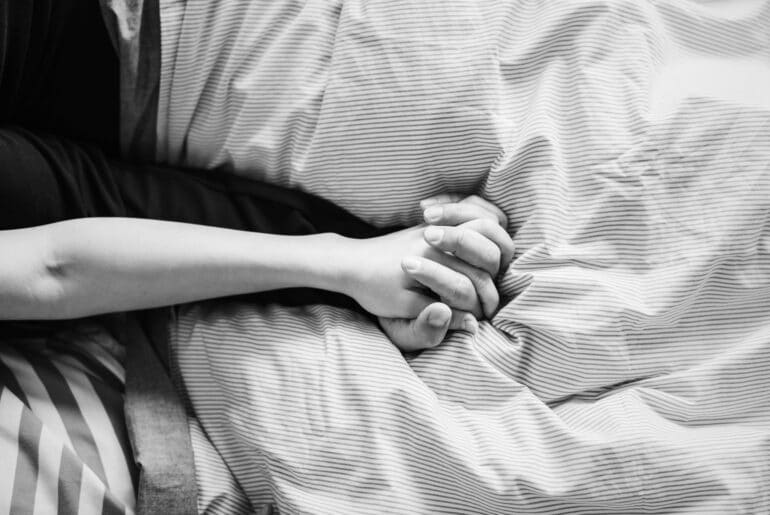 close up of couple holding hands in bed